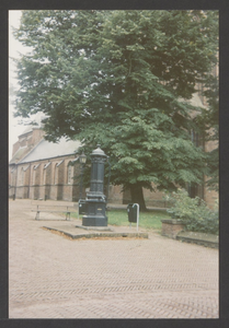  De achtkantige gietijzeren pomp met zitbank en papierbak, op de achtergrond de St. Andrieskerk.