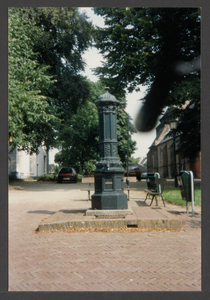  De achtkantige gietijzeren pomp met zitbank en papierbak, op de achtergrond de St. Andrieskerk.