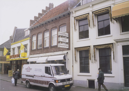  De voorgevel van Van Schuppen tapijt en slaapkamers. Voor de gevel staat een bestelbus en lopen enkele voetgangers. ...