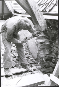  Een bouwvakker zaagt in een oude balk in de kap tijdens de restauratie van het woonhuis.
