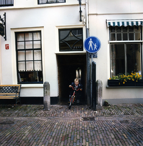  Gezicht door de doorgang naar de Mazijk, waaruit een jongetje op de fiets staat. Links 't Koffiehuis 'de Mazijk' en ...