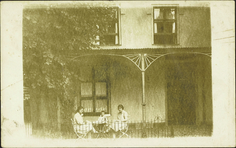  Gedeelte van de voorgevel van café Dorpszicht met drie mensen zittend aan een tafeltje onder de luifel.