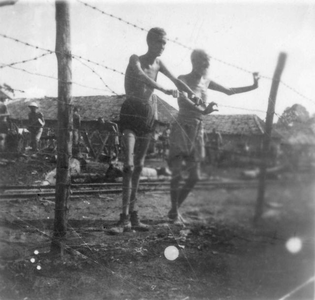 Twee burgergeïnterneerden bij de prikkeldraadomheining van kamp Si Rengorengo. Foto van J.P.J. Kosak, 1945.<br/>NIOD 100438 <a class=uline href=http://www.beeldbankwo2.nl target=_blank>Beeldbank WO2</a>