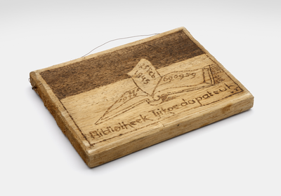 Small wooden board with a book and the text &quot;Bibliotheek Tjikoedapateuh&quot; (Library Tjikoedapateuh), made to commemmorate the one year existence of the library in the 15th Battallion's Encampment in Bandung.&lt;br/&gt;NIOD Collectie 417-089a