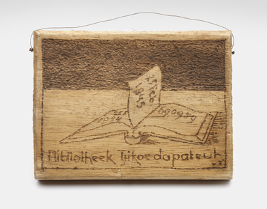 Een houten plankje met daarop een opengeslagen boek en de tekst &quot;Bibliotheek Tjikoedapateuh&quot;, gemaakt ter gelegenheid van het eenjarig bestaan van de bibliotheek in het Kampement 15de Bat. in Bandoeng.&lt;br/&gt;NIOD Collectie 417-089b